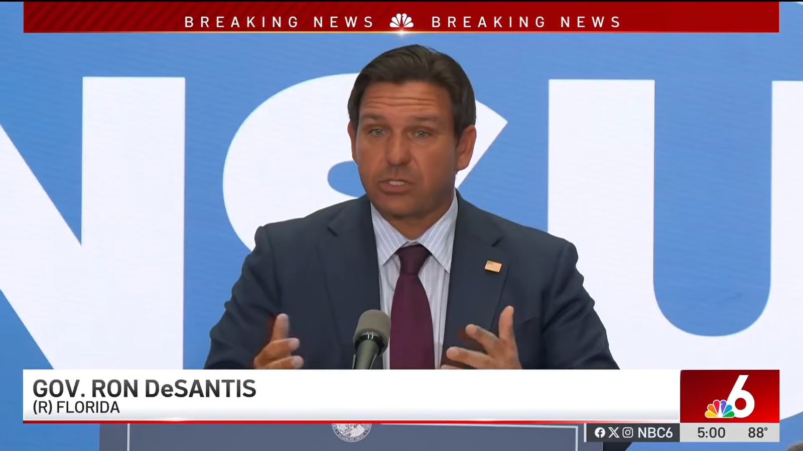 Governador Ron DeSantis fala em coletiva, com chyron 'BREAKING NEWS' da NBC ao fundo
