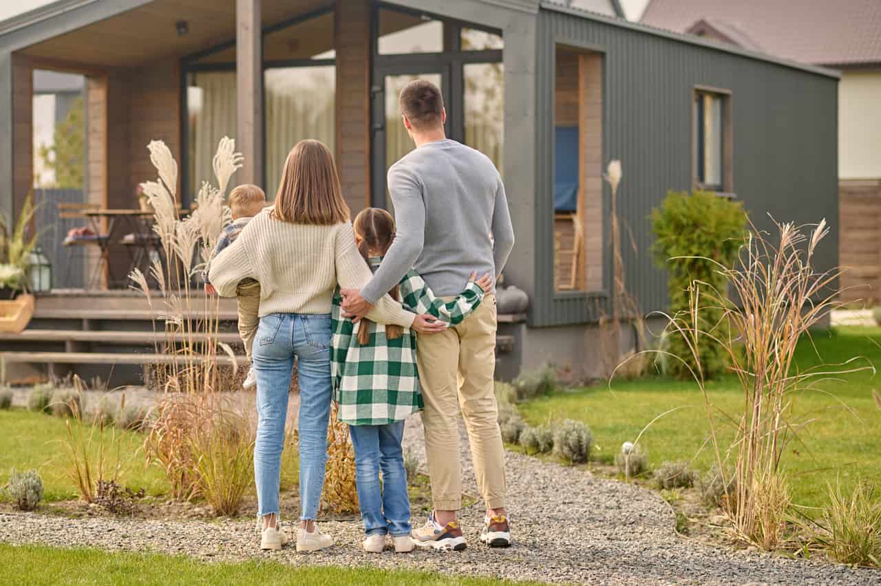 Família observando fachada de casa nova, de costas, em quintal gramado