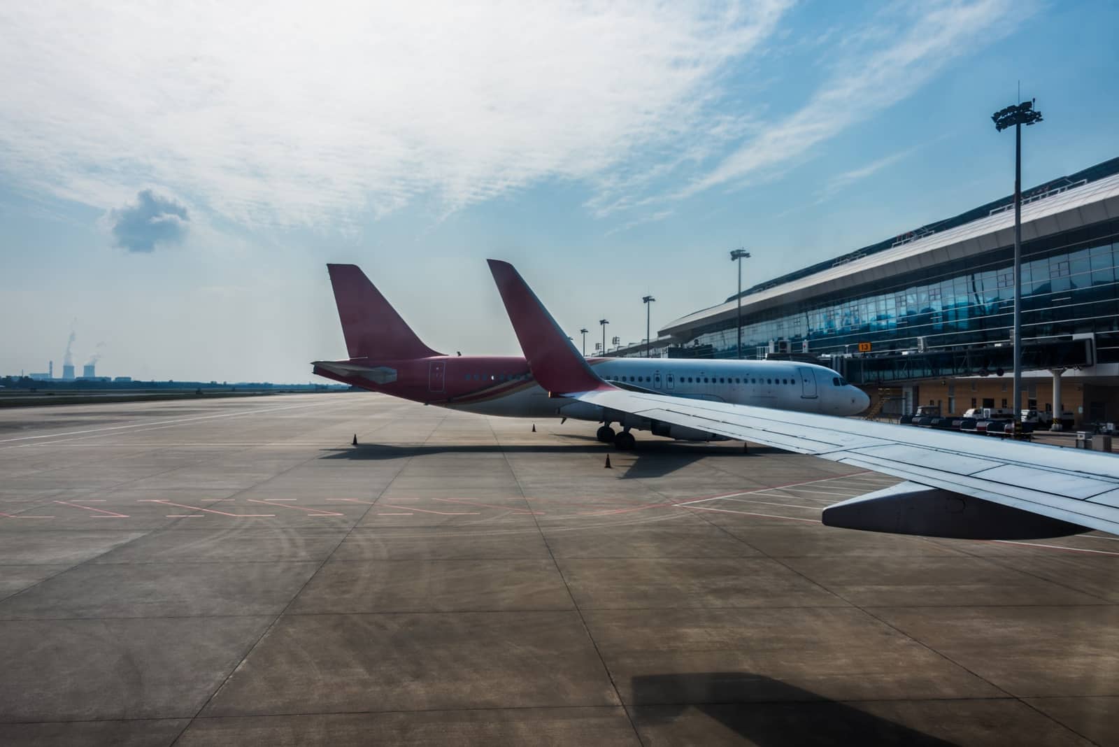 Vista da asa de um avião estacionado em pátio de aeroporto, com terminal ao fundo