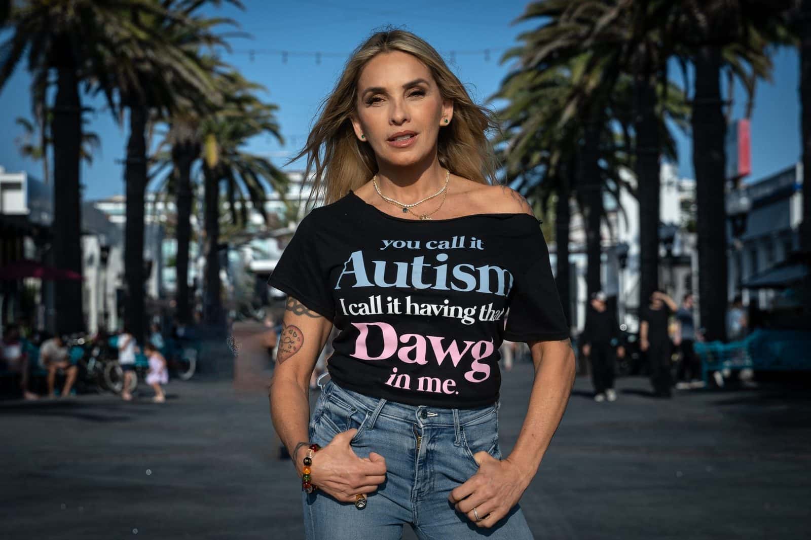 Syang em calçadão com palmeiras na Califórnia, vestindo camiseta com mensagem sobre autismo