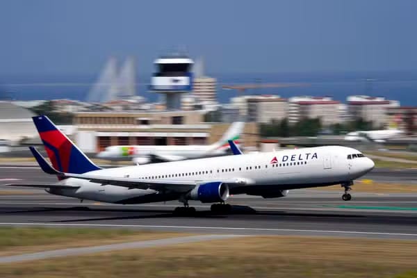 Avião de fuselagem larga da Delta Air Lines, branco com cauda azul e vermelha, toca a pista de um aeroporto com torre de controle ao fundo