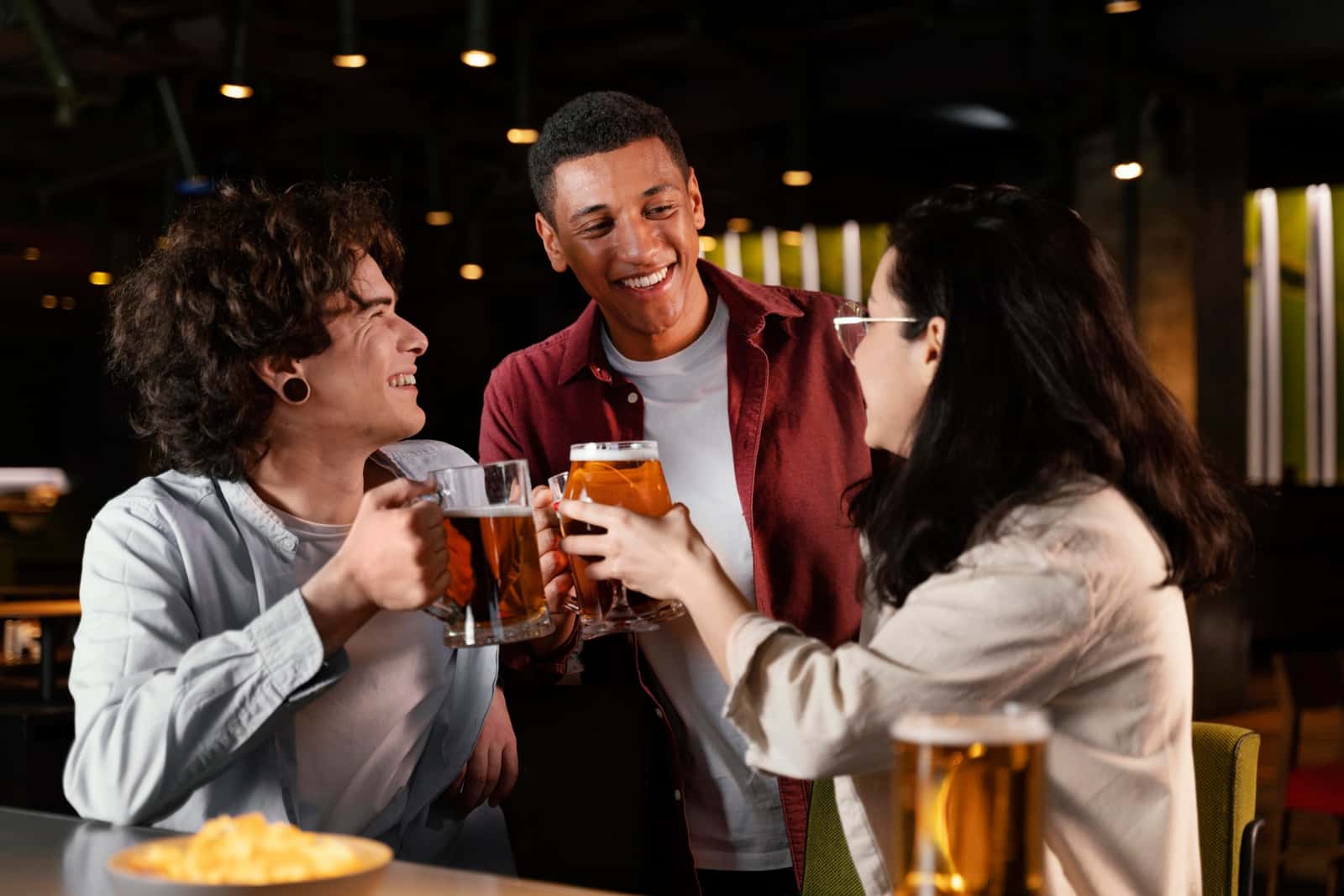 Três amigos brindando com canecas de cerveja em um bar