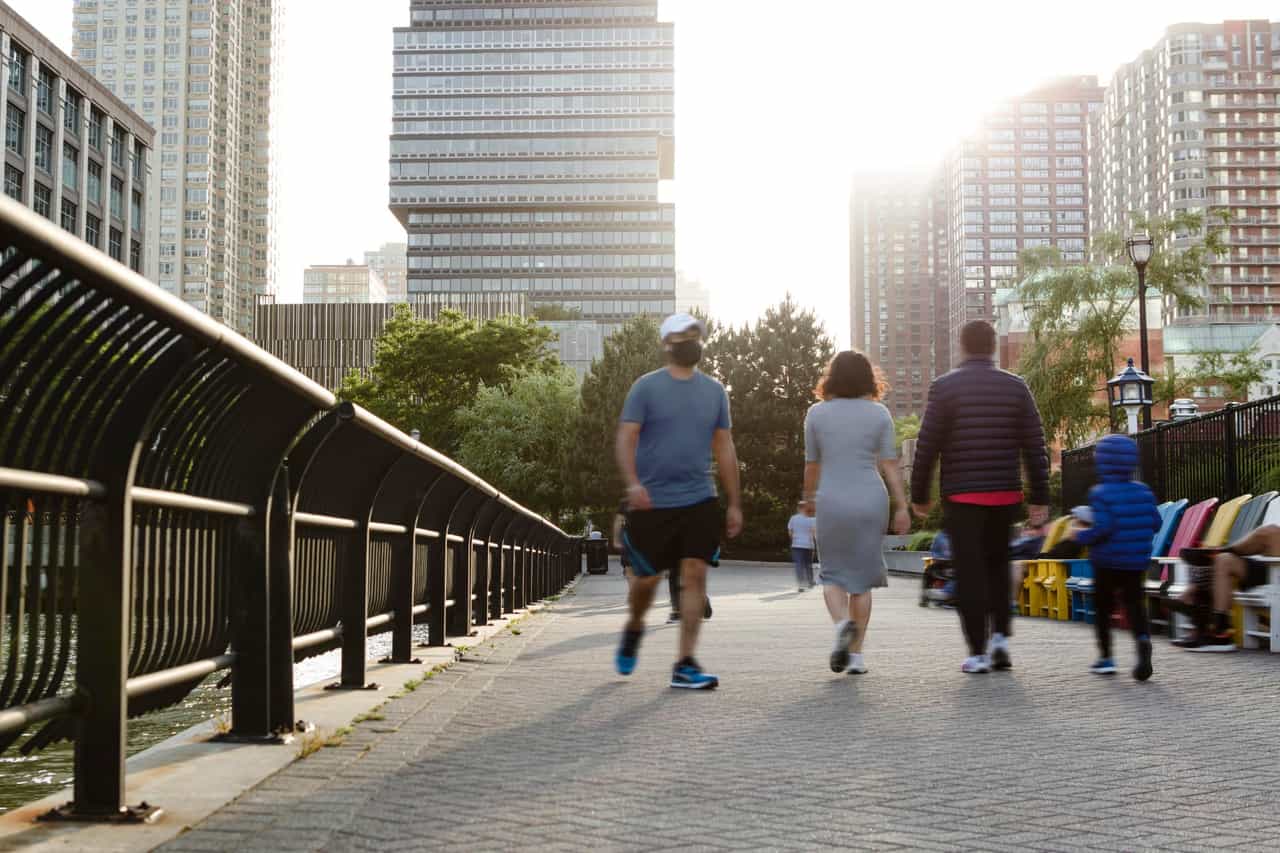 Pessoas caminhando por um calçadão urbano ao entardecer, com prédios altos ao fundo