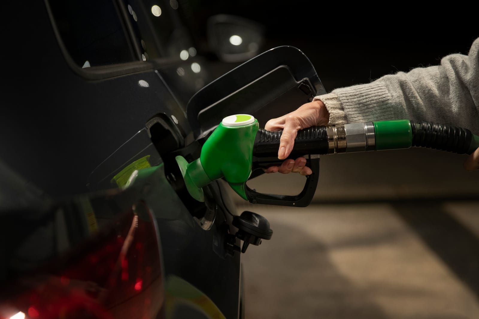 Mão segura a pistola de combustível verde abastecendo um carro escuro à noite