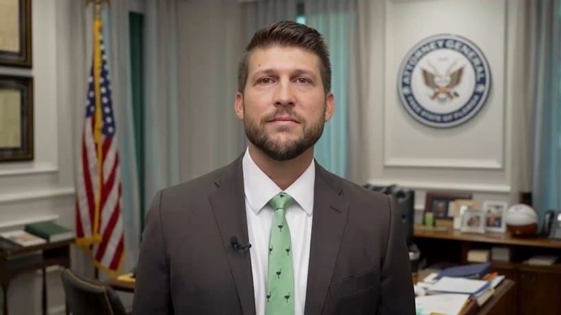 James Uthmeier, procurador-geral da Flórida, de terno cinza e gravata verde, fala em seu gabinete, entre a bandeira dos Estados Unidos e o selo do cargo na parede