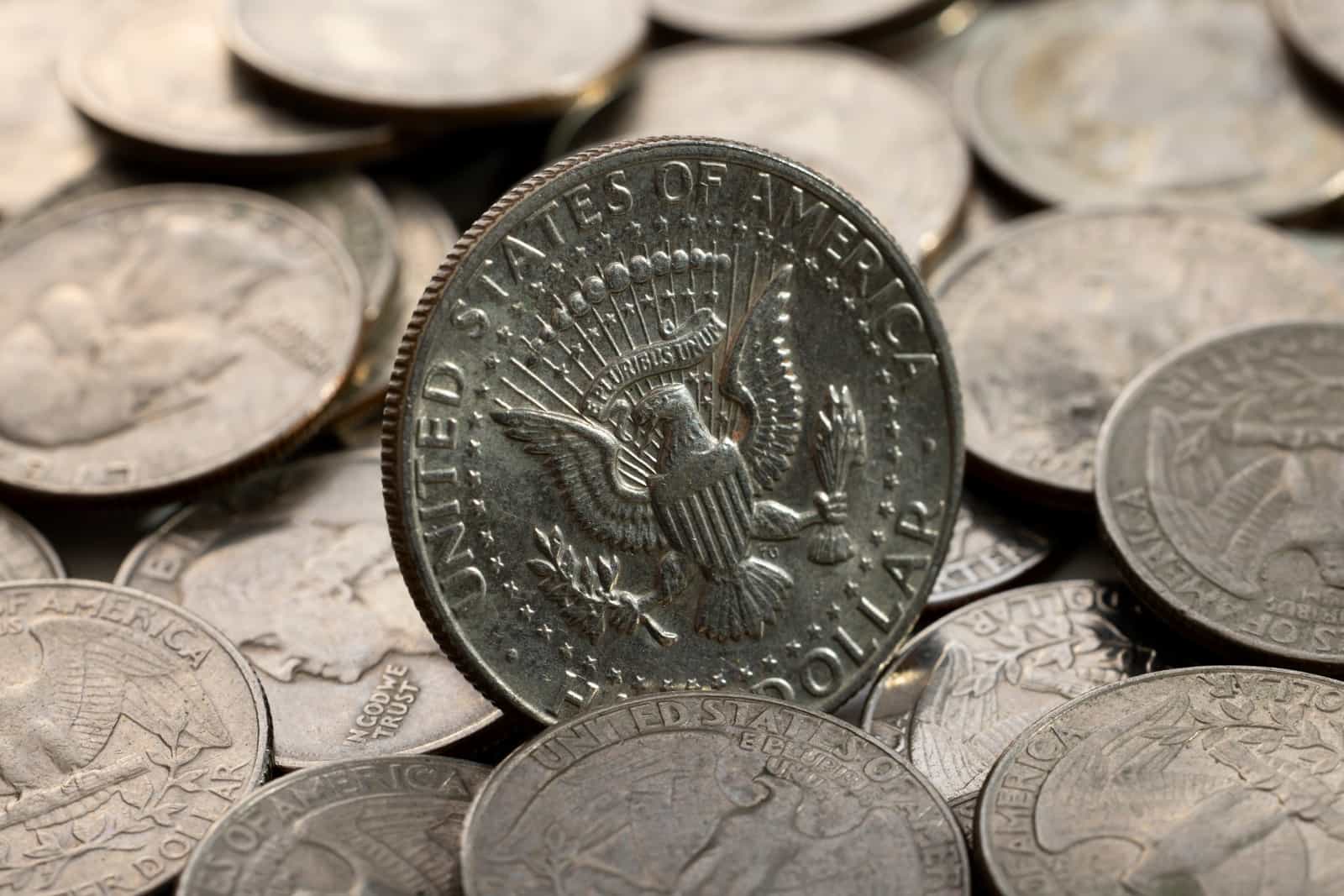 Pilha de moedas americanas em close, com moeda de meio dólar em destaque
