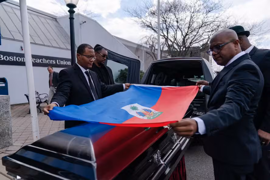 Dois homens de terno estendem a bandeira do Haiti sobre um caixão durante um funeral