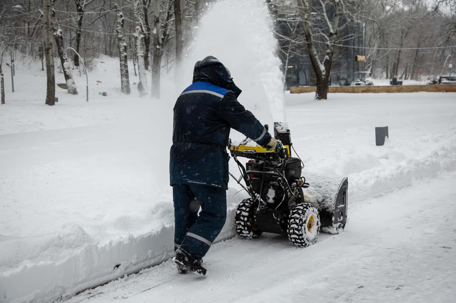 Trabalhador de agasalho azul operando limpa-neve em calçada coberta de neve