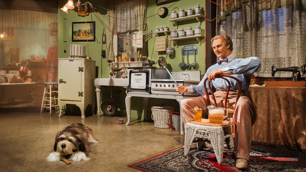 Cena do Carousel of Progress com o Audio-Animatronic do pai, John, sentado em cadeira ao lado do cachorro Rover em cozinha de época