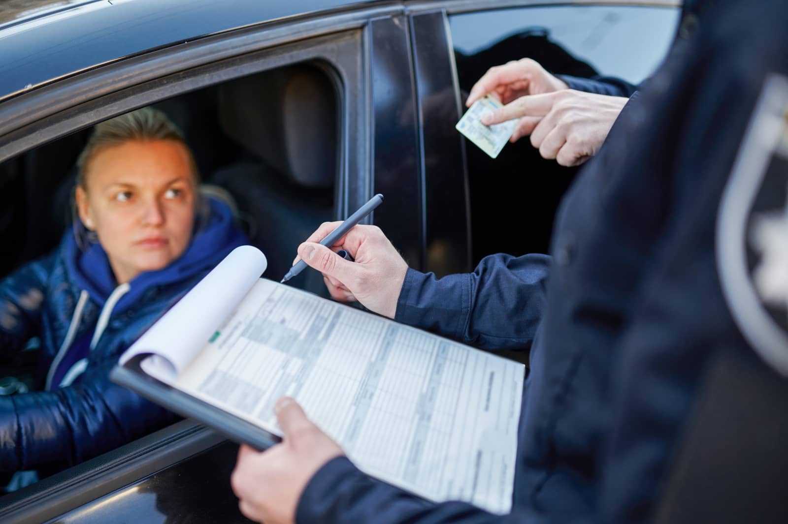 Policial anota em prancheta e mostra documento a motorista em carro durante abordagem de trânsito
