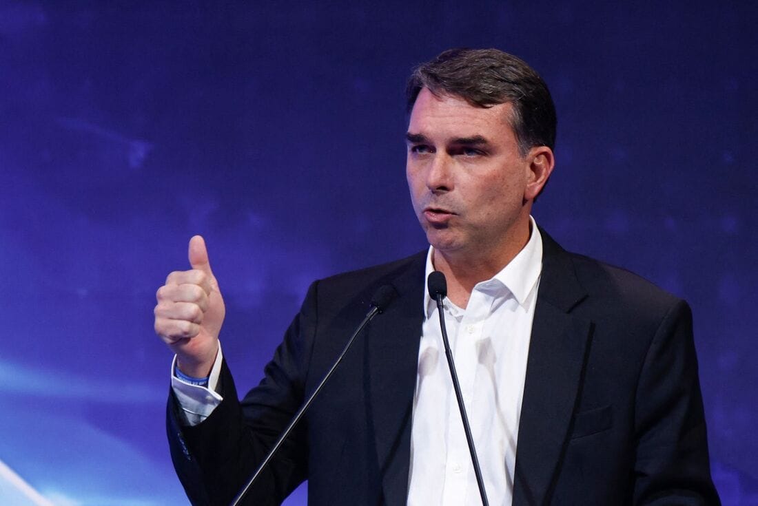 O senador Flávio Bolsonaro discursa ao microfone, de terno escuro, fazendo sinal de positivo com a mão