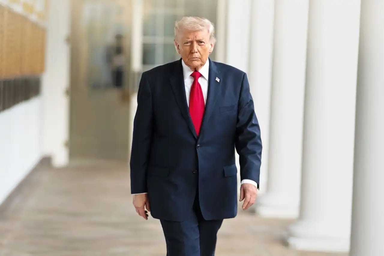Donald Trump caminha pela colunata da Casa Branca, de terno azul-marinho e gravata vermelha