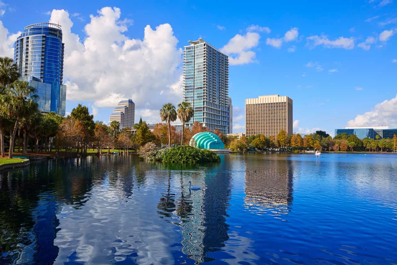 Vista de um lago urbano cercado por prédios altos e palmeiras em dia ensolarado