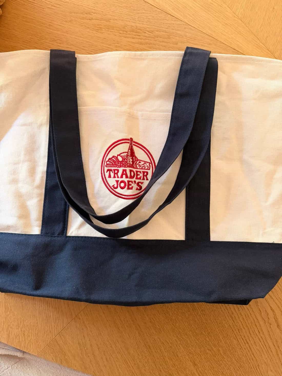Sacola de compras reutilizável com o logo do Trader Joe's, alças azuis sobre fundo de madeira
