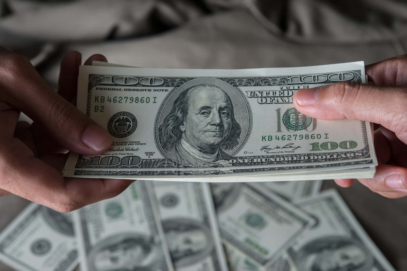 Mão segurando notas de cem dólares americanos