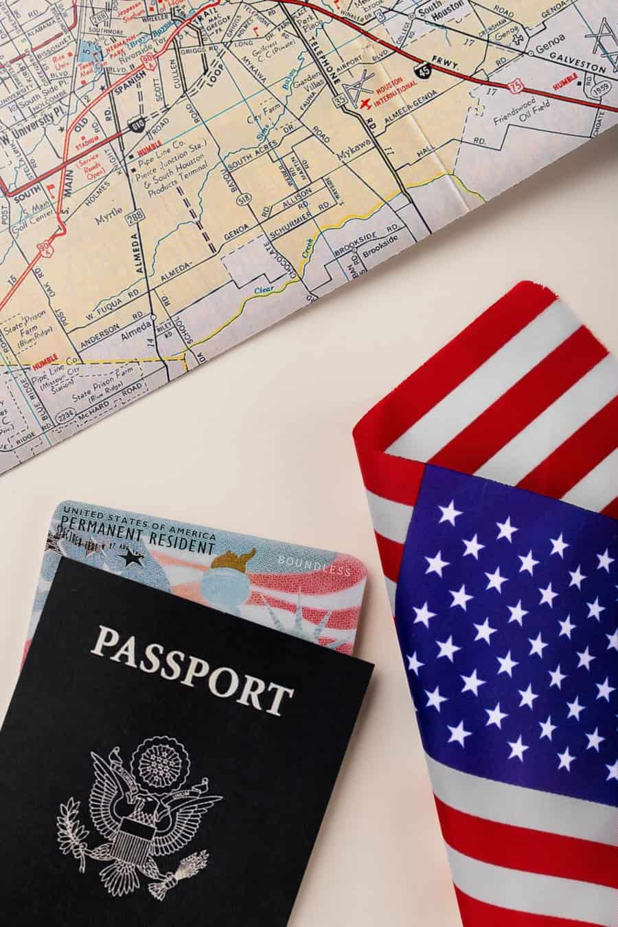 Passaporte, cartão de residente permanente e bandeira dos Estados Unidos sobre mesa, ao lado de um mapa