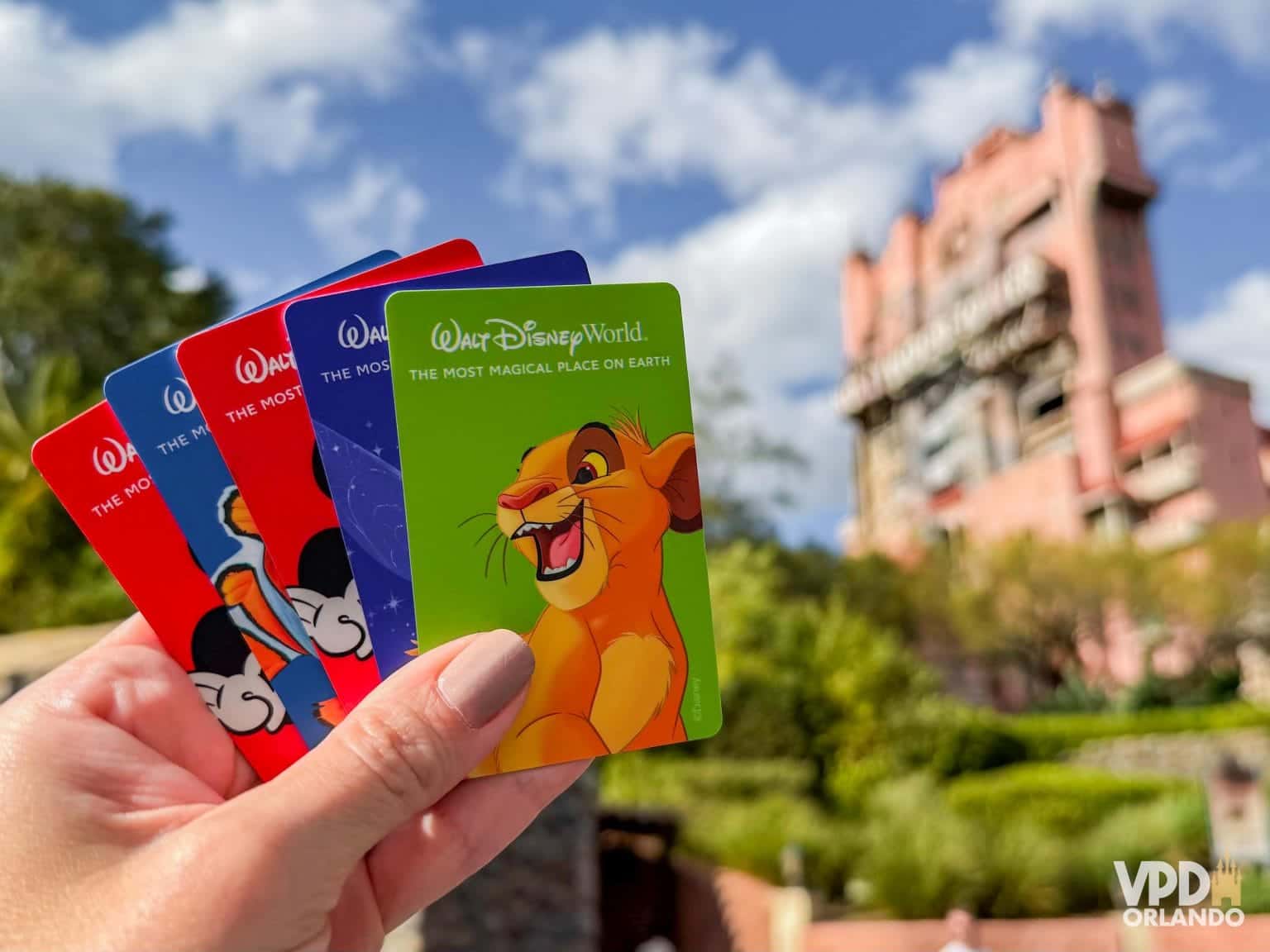 Mão segura cartões coloridos do Walt Disney World, com a Tower of Terror ao fundo