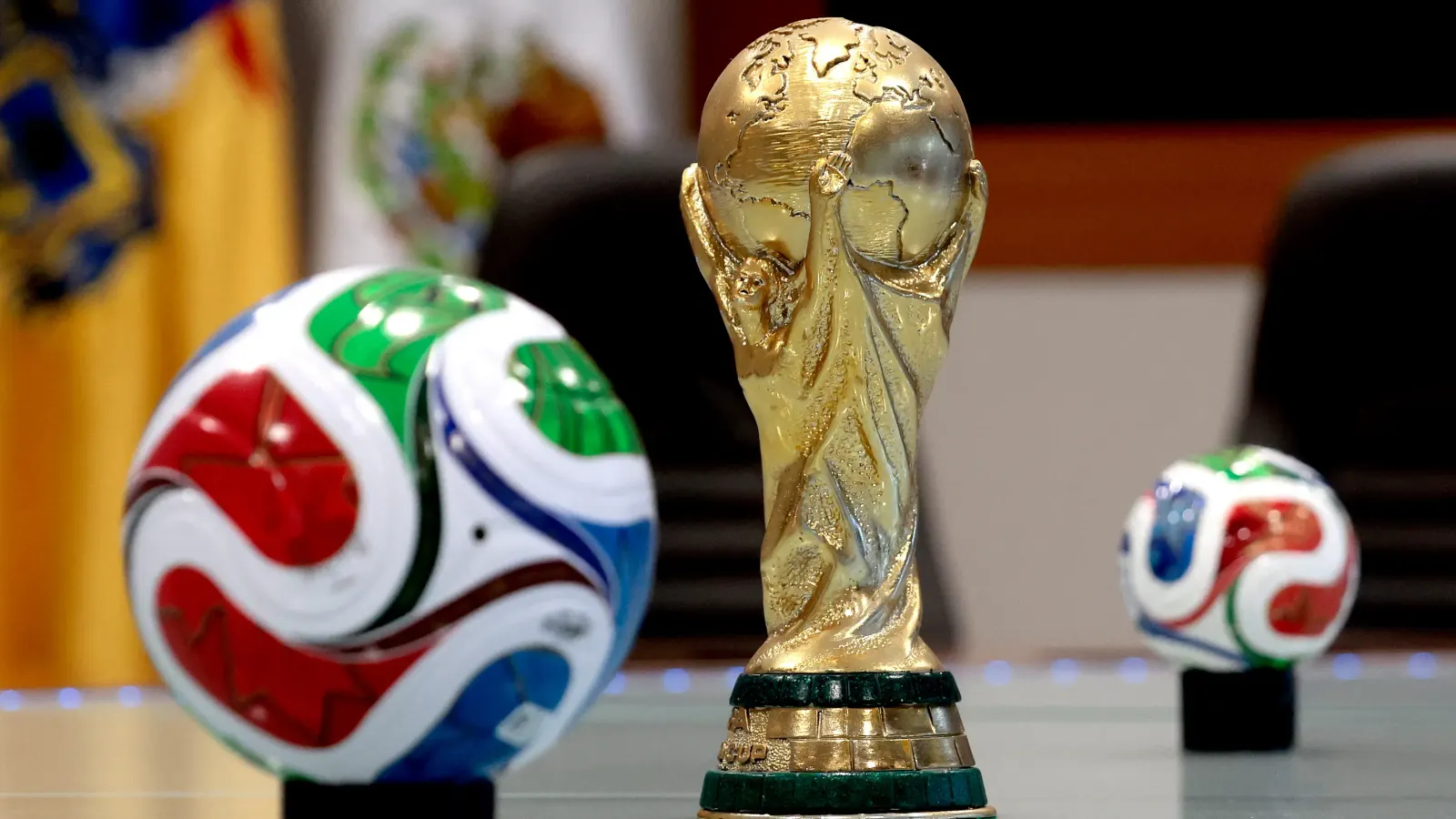 Taça da Copa do Mundo ao lado de bolas oficiais sobre uma mesa