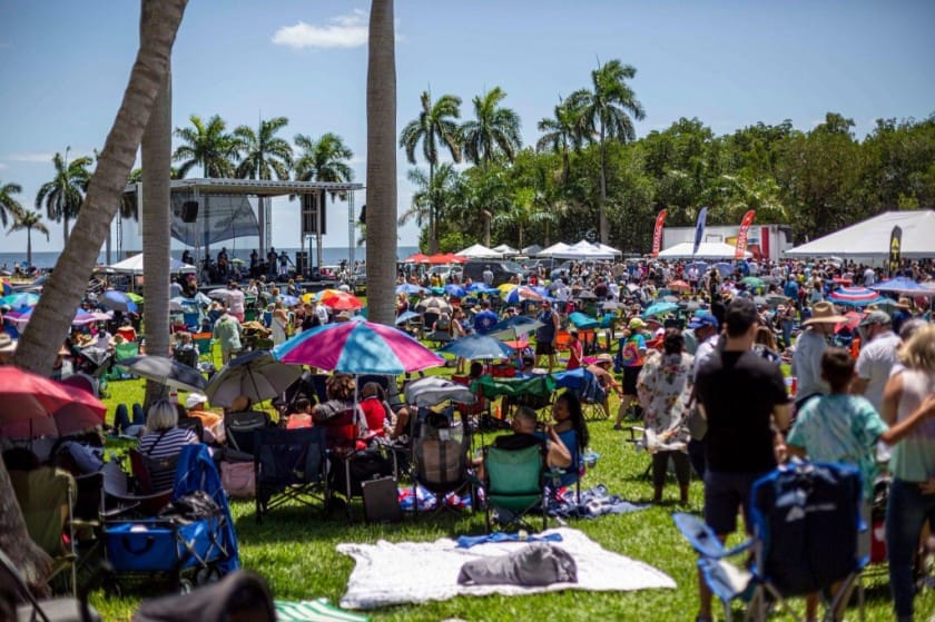 Multidão em um festival ao ar livre na Flórida, com palmeiras e palco ao fundo