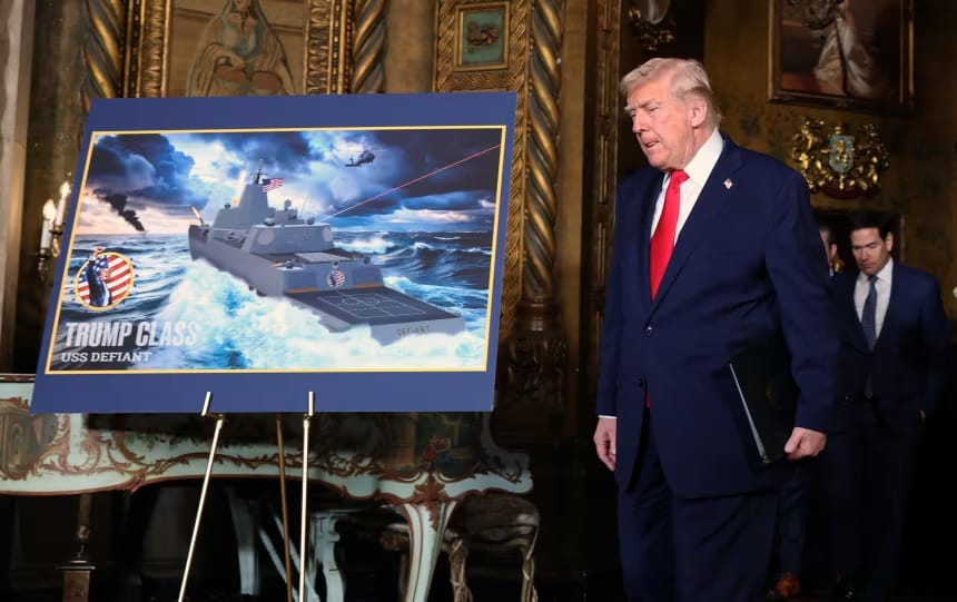Presidente dos Estados Unidos caminha ao lado de um cavalete com a ilustração de um navio de guerra cinzento em alto-mar e os dizeres Trump Class USS Defiant
