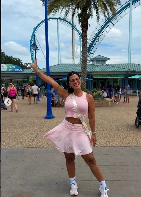 Jovem sorridente em parque temático, acenando com o braço levantado
