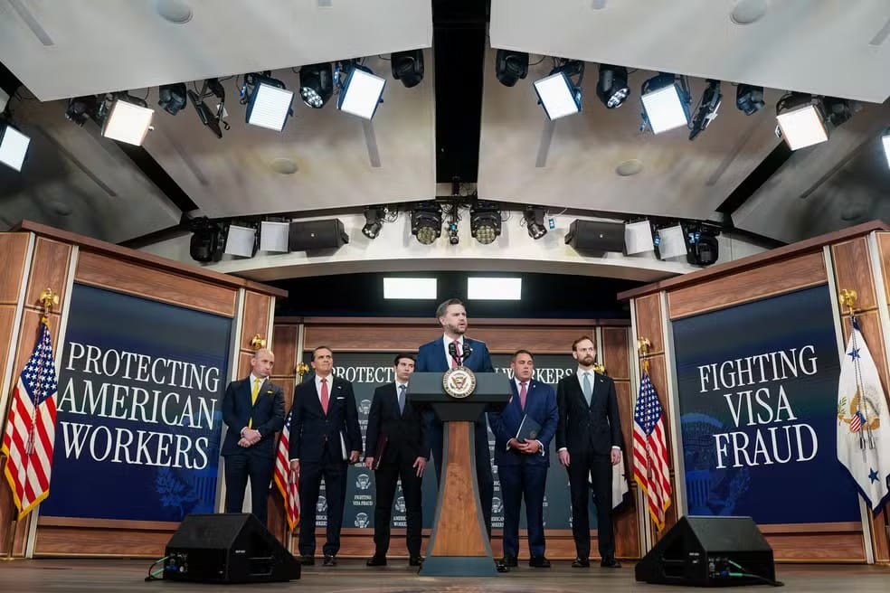 Autoridades em pé diante de dois painéis com os dizeres Protecting American Workers e Fighting Visa Fraud, em coletiva de imprensa