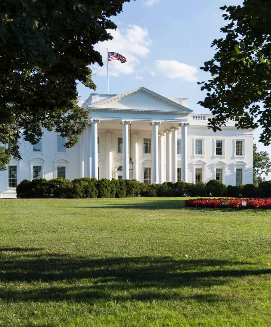 Fachada da Casa Branca, em Washington, vista entre árvores, com bandeira dos Estados Unidos no topo