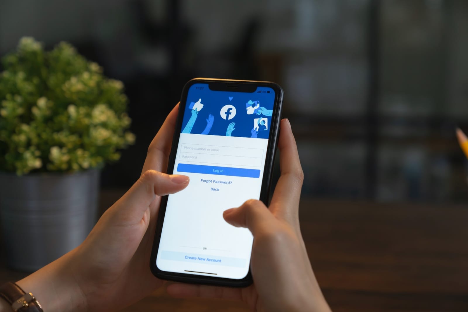 Mão segurando um celular com a tela de login do aplicativo Facebook