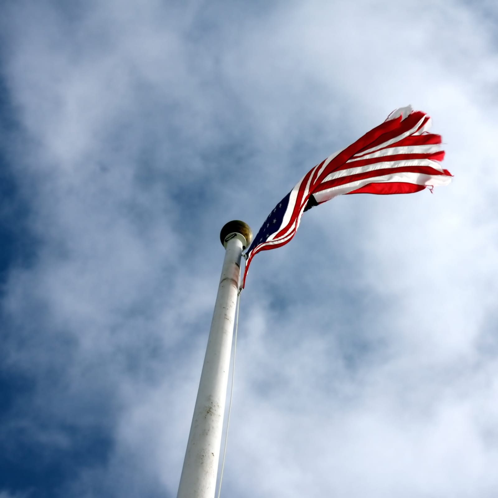 Bandeira dos Estados Unidos esfiapada tremulando em um mastro branco contra o céu nublado