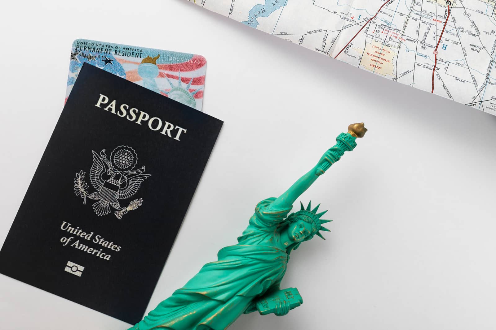 Passaporte americano com um green card atrás, ao lado de uma miniatura da Estátua da Liberdade e de um mapa