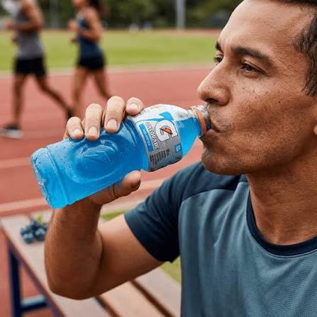 Homem bebe uma garrafa de Gatorade azul ao lado de uma pista de corrida