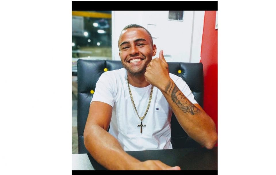Homem de camiseta branca, corrente e crucifixo dourados, sorri e faz sinal de positivo com a mão em foto de arquivo pessoal fornecida pela família