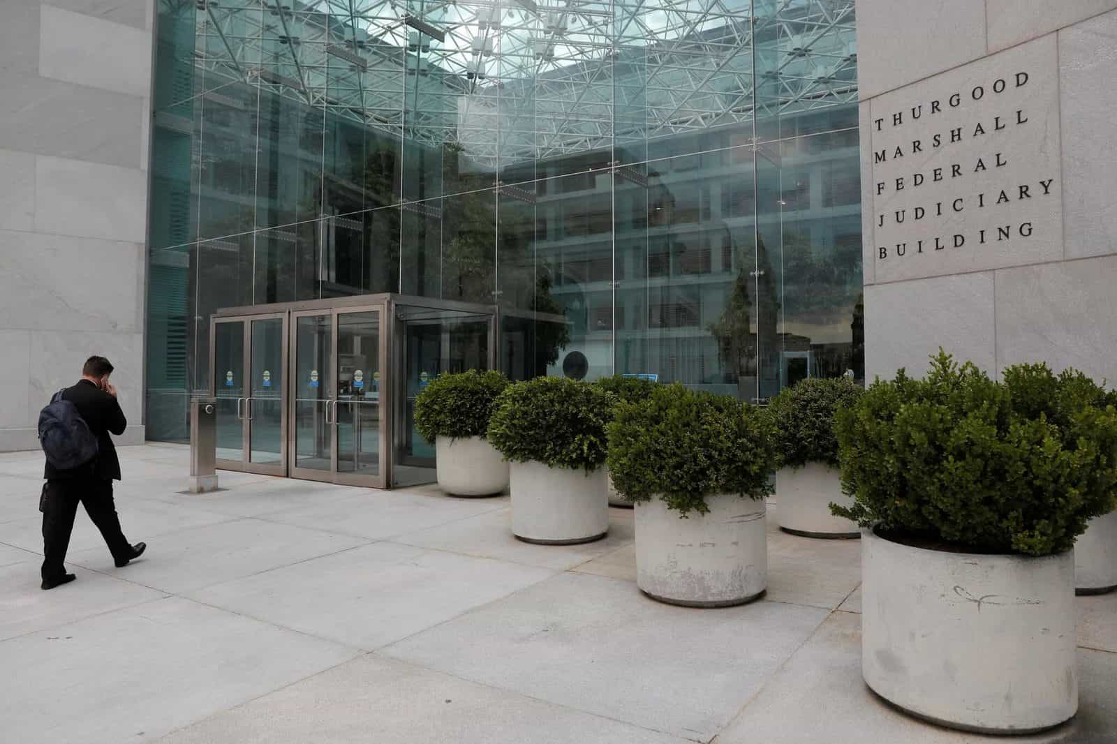 Fachada de prédio de granito com átrio de vidro e a inscrição Thurgood Marshall Federal Judiciary Building, com homem caminhando ao telefone em primeiro plano