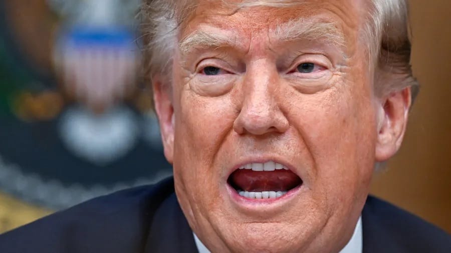 Close-up do presidente Donald Trump falando, de terno escuro, com o selo presidencial desfocado ao fundo