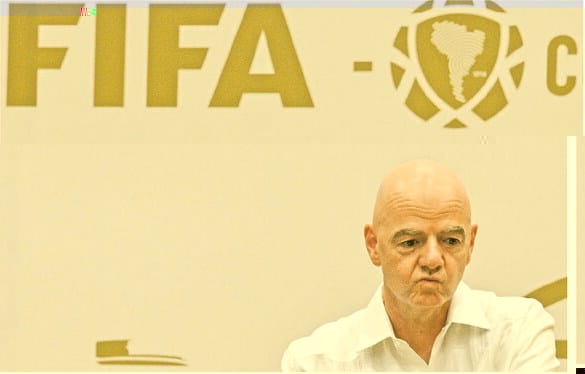 Gianni Infantino, de camisa branca, sentado com expressão fechada diante de um painel com os logotipos da FIFA e da Conmebol