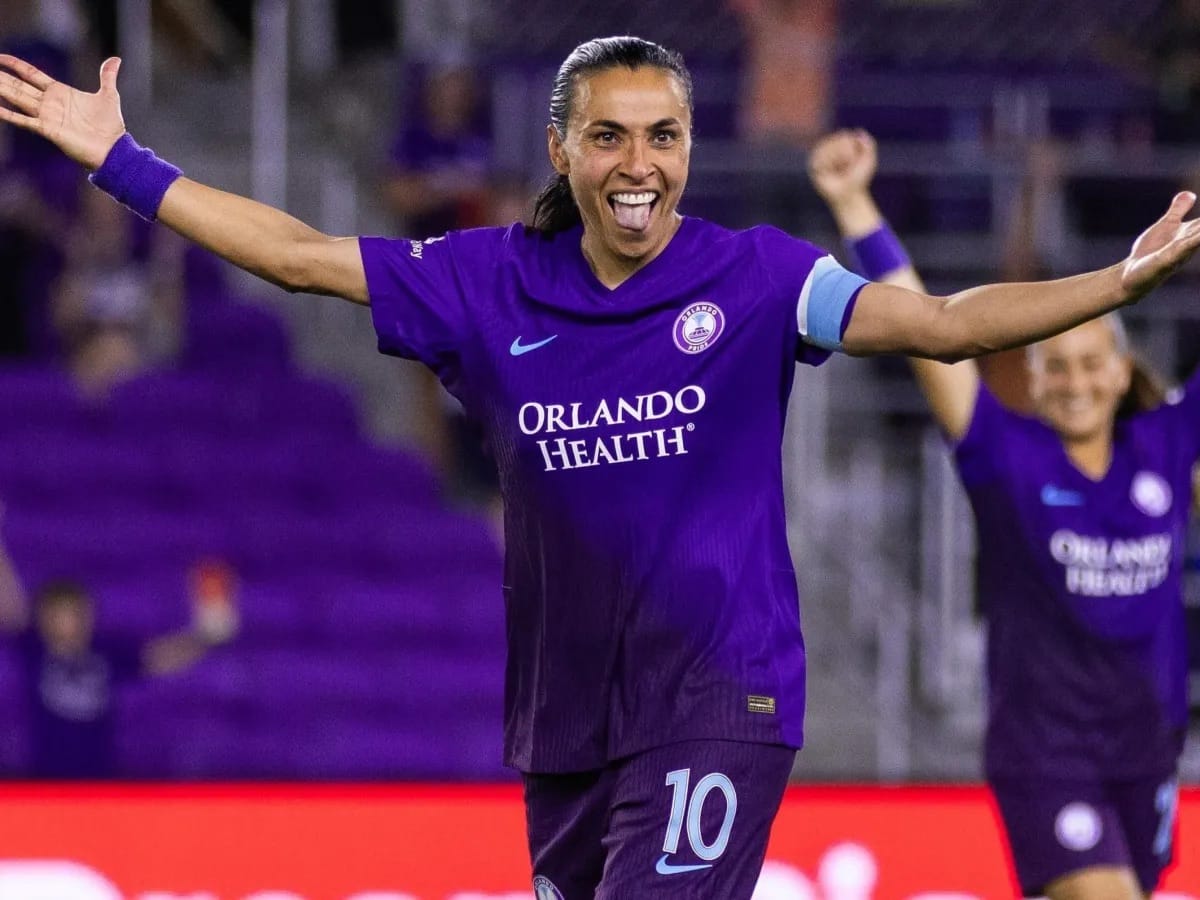 Jogadora com a camisa roxa número 10 do Orlando Pride comemora de braços abertos, com uma companheira festejando ao fundo