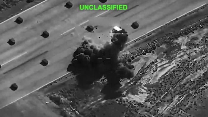 Imagem aérea militar em preto e branco marcada como UNCLASSIFIED, mostrando a explosão e a nuvem de fumaça de um ataque a um alvo em solo