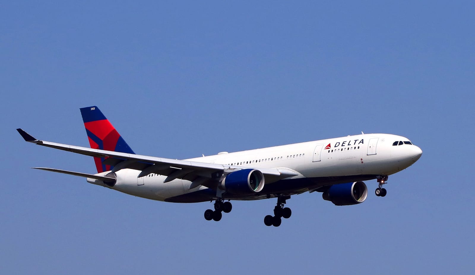 Avião comercial branco da Delta Air Lines com a cauda em azul e vermelho, em aproximação final com o trem de pouso baixado, contra o céu azul