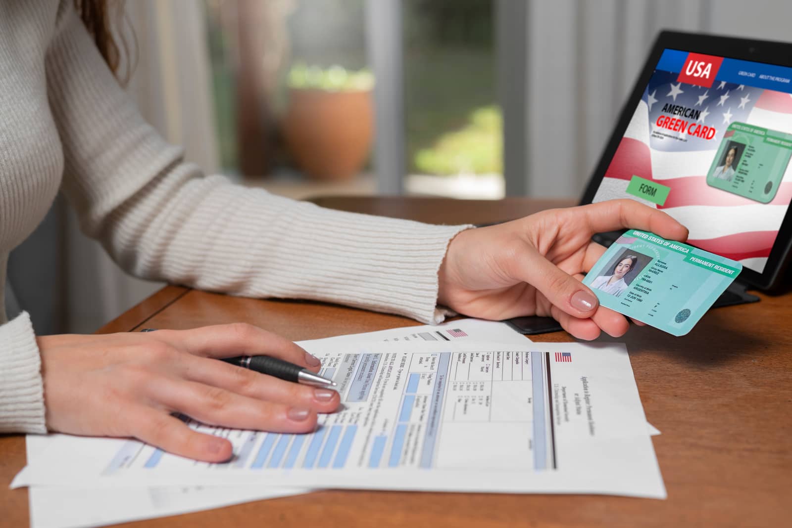 Mulher segurando um green card ao lado de formulário de imigração americano e tablet