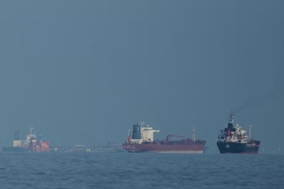 Três navios-tanque de petróleo ancorados em mar aberto, sob céu e água em tons de cinza-azulado, cenário associado ao Estreito de Ormuz