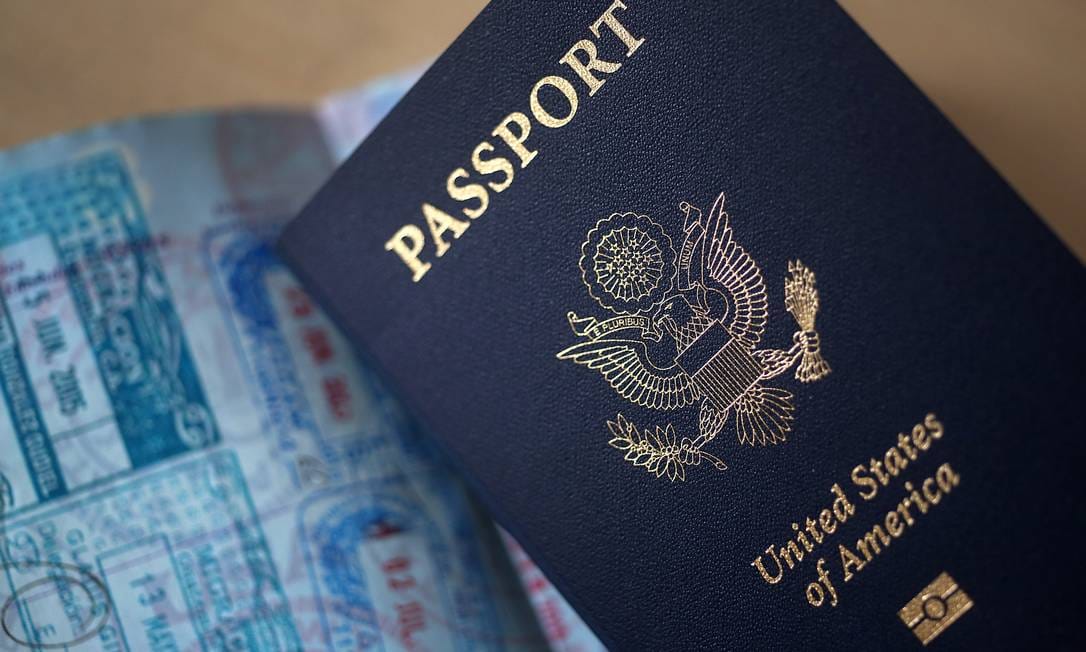 Passaporte azul-escuro dos Estados Unidos fechado sobre as páginas de outro passaporte cobertas de selos de entrada e saída