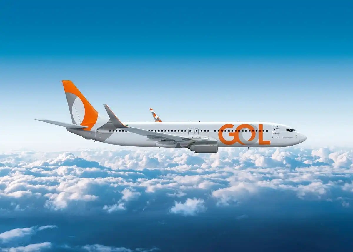 Avião da Gol em voo acima de um mar de nuvens, sob um céu azul