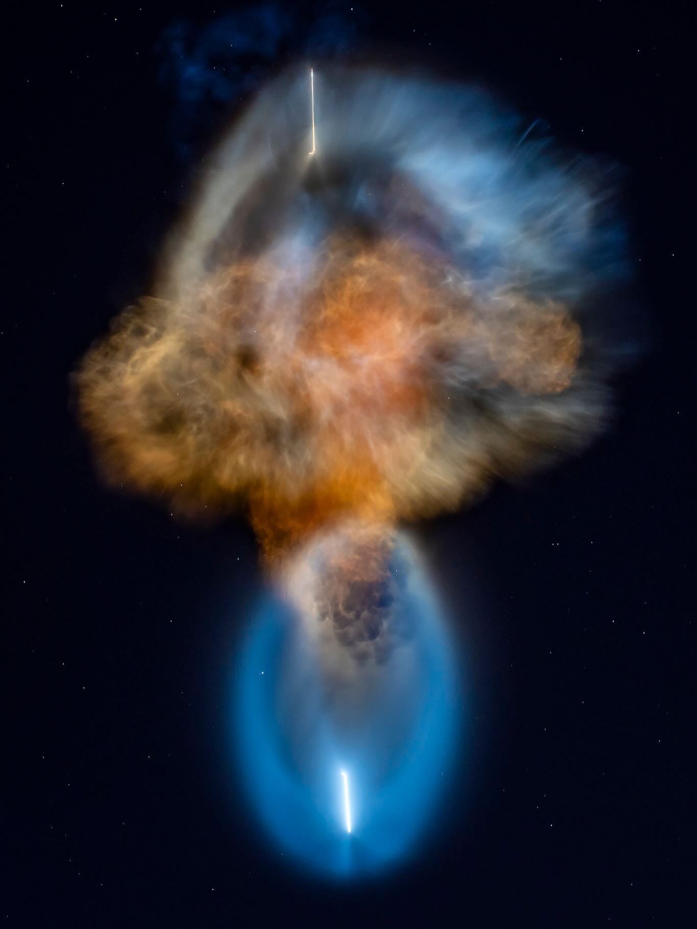Nuvem colorida em tons de laranja, azul e branco, formada pelo escapamento de um foguete, no céu escuro com estrelas