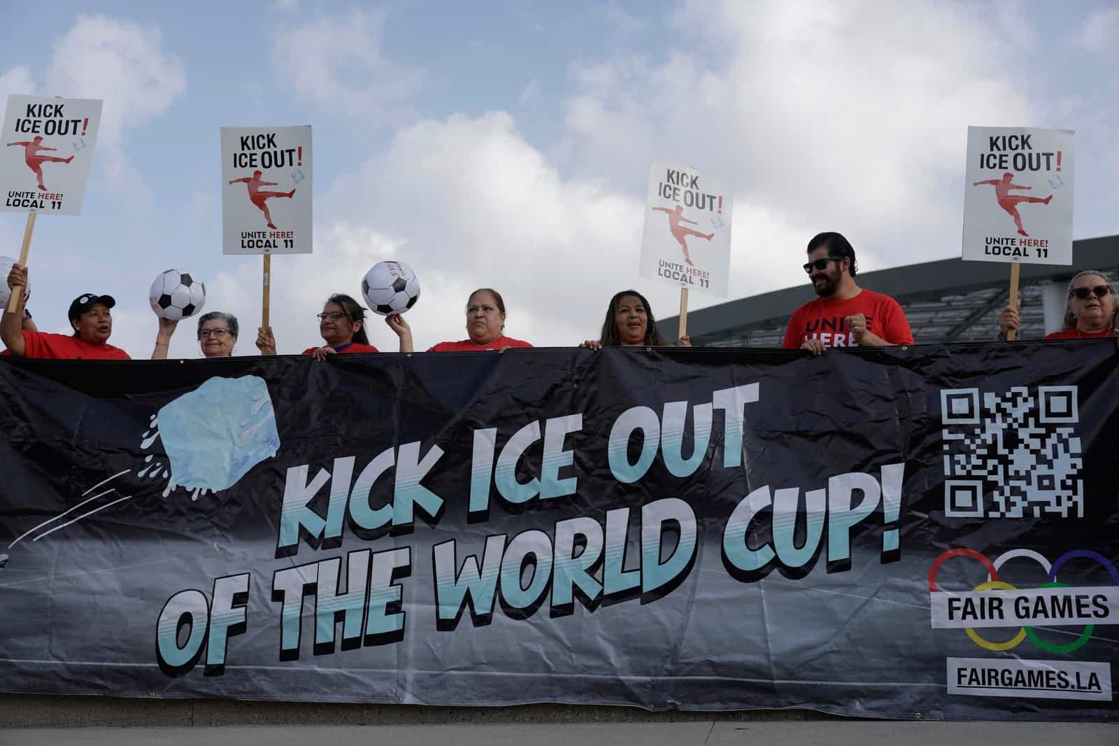 Manifestantes com camisetas vermelhas seguram bolas de futebol, cartazes e uma grande faixa preta com a frase Kick ICE Out of the World Cup em protesto perto de um estádio