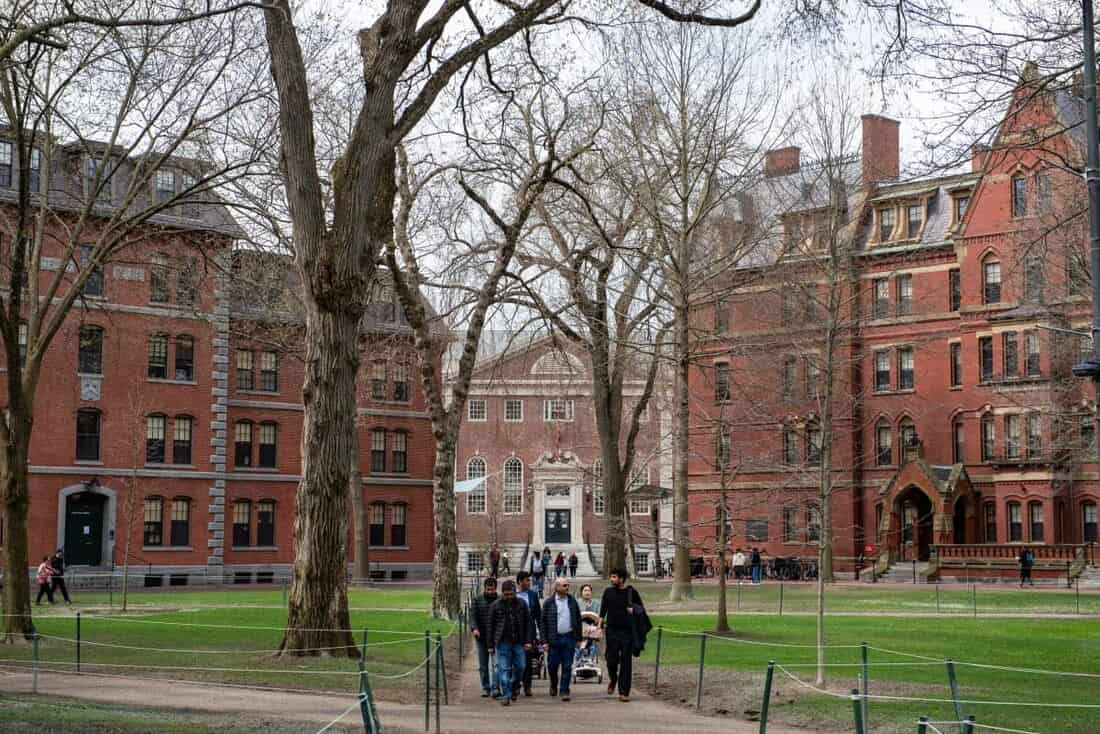 Pedestres caminham por alameda entre os prédios de tijolo vermelho e as árvores sem folhas do pátio central de Harvard