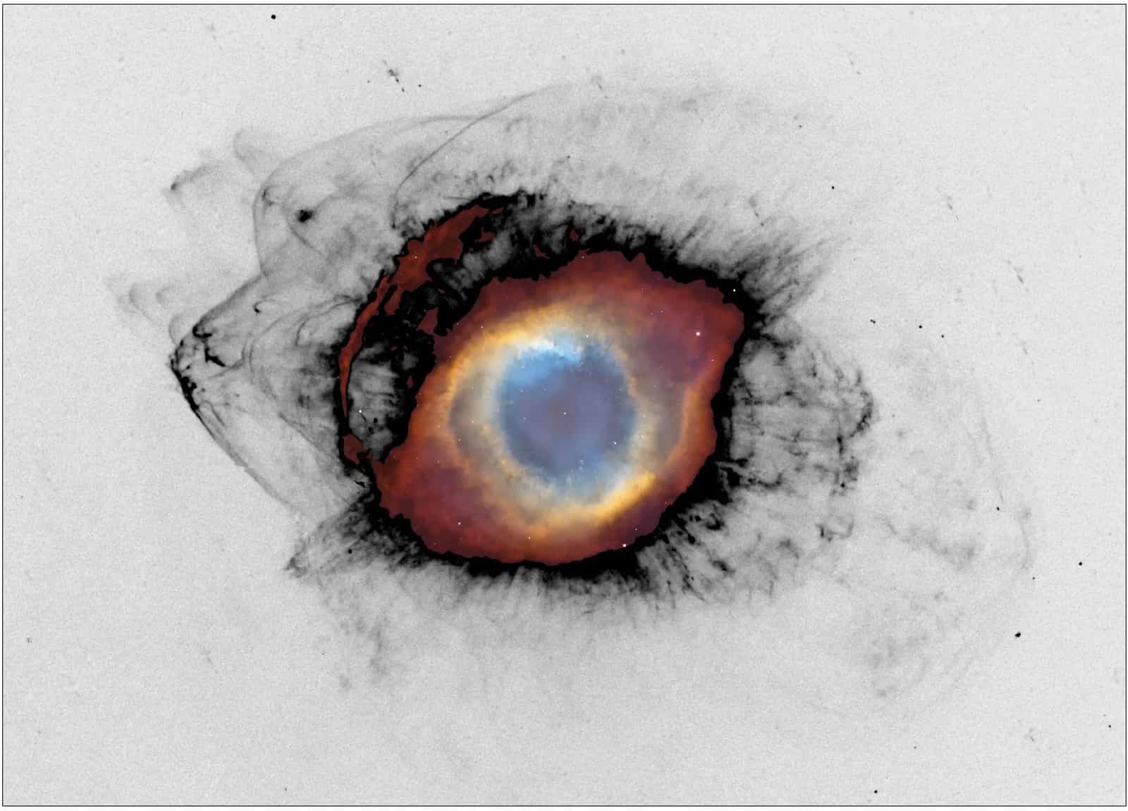 Imagem astronômica em tons invertidos da Nebulosa Hélice, com o anel central azul e alaranjado cercado por faixas escuras e difusas de detritos