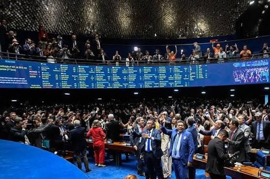 Plenário do Senado lotado, com parlamentares de braços levantados e o painel de votação aceso ao fundo