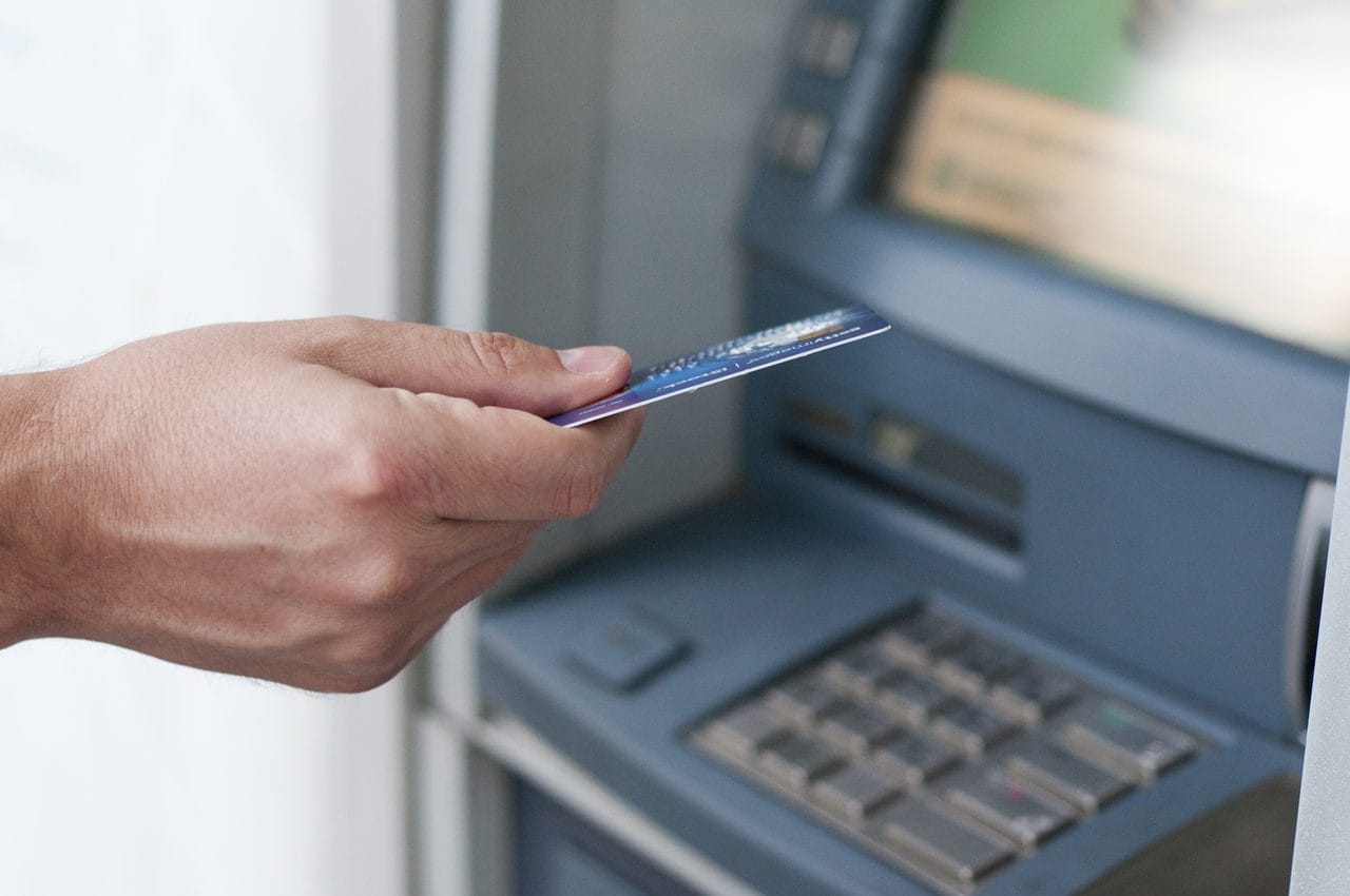 Mão de um homem inserindo um cartão azul em um caixa eletrônico de banco