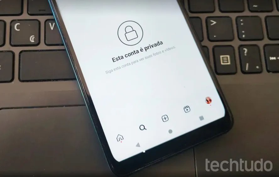 Celular sobre um teclado de notebook mostrando a tela de uma conta privada em rede social, com o ícone de cadeado