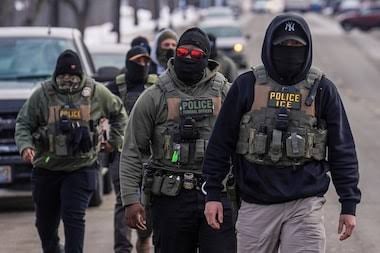 Agentes de coletes escritos Police e ICE, com rostos cobertos, caminham em uma rua nevada